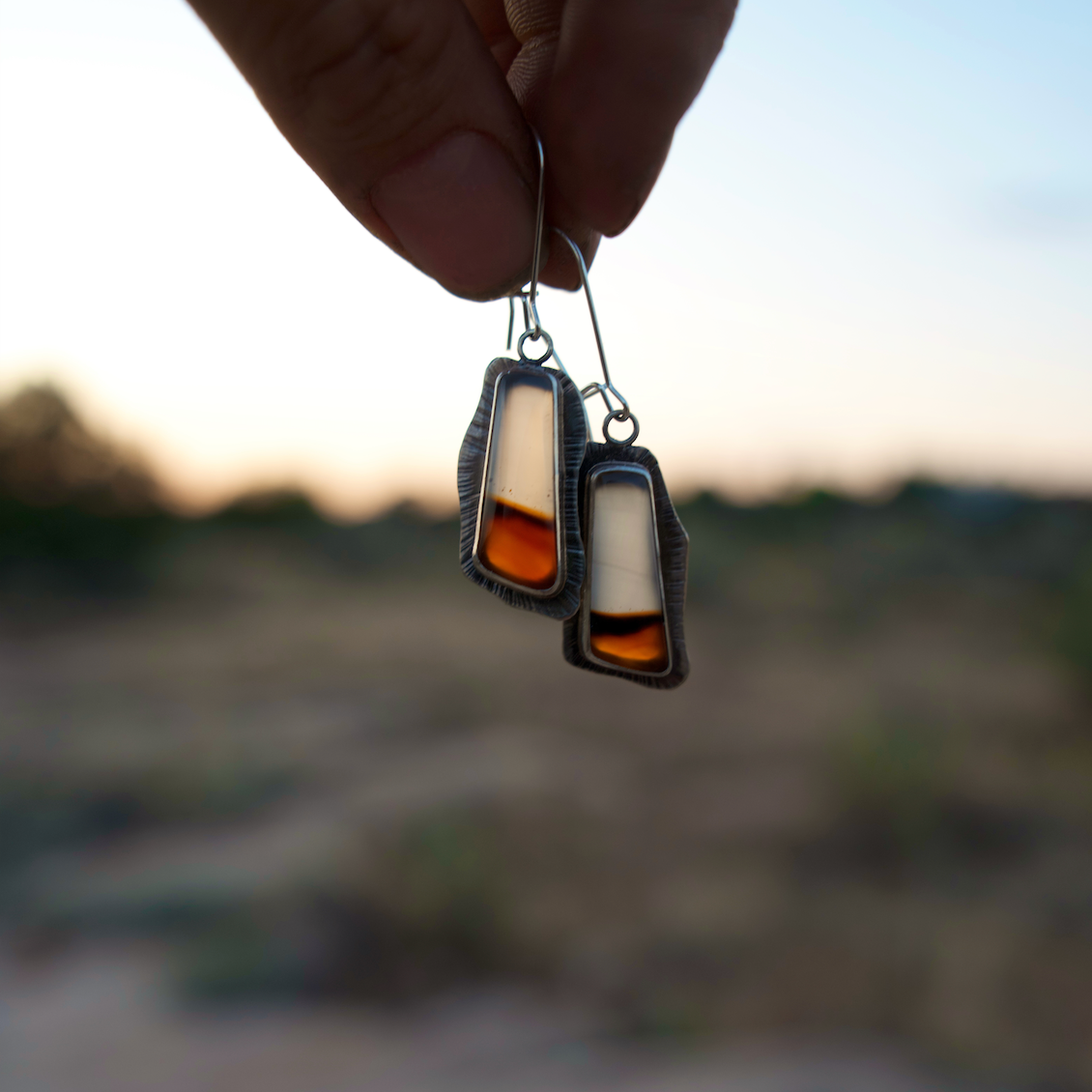 Hand holding a pair of earrings with a blurred natural background