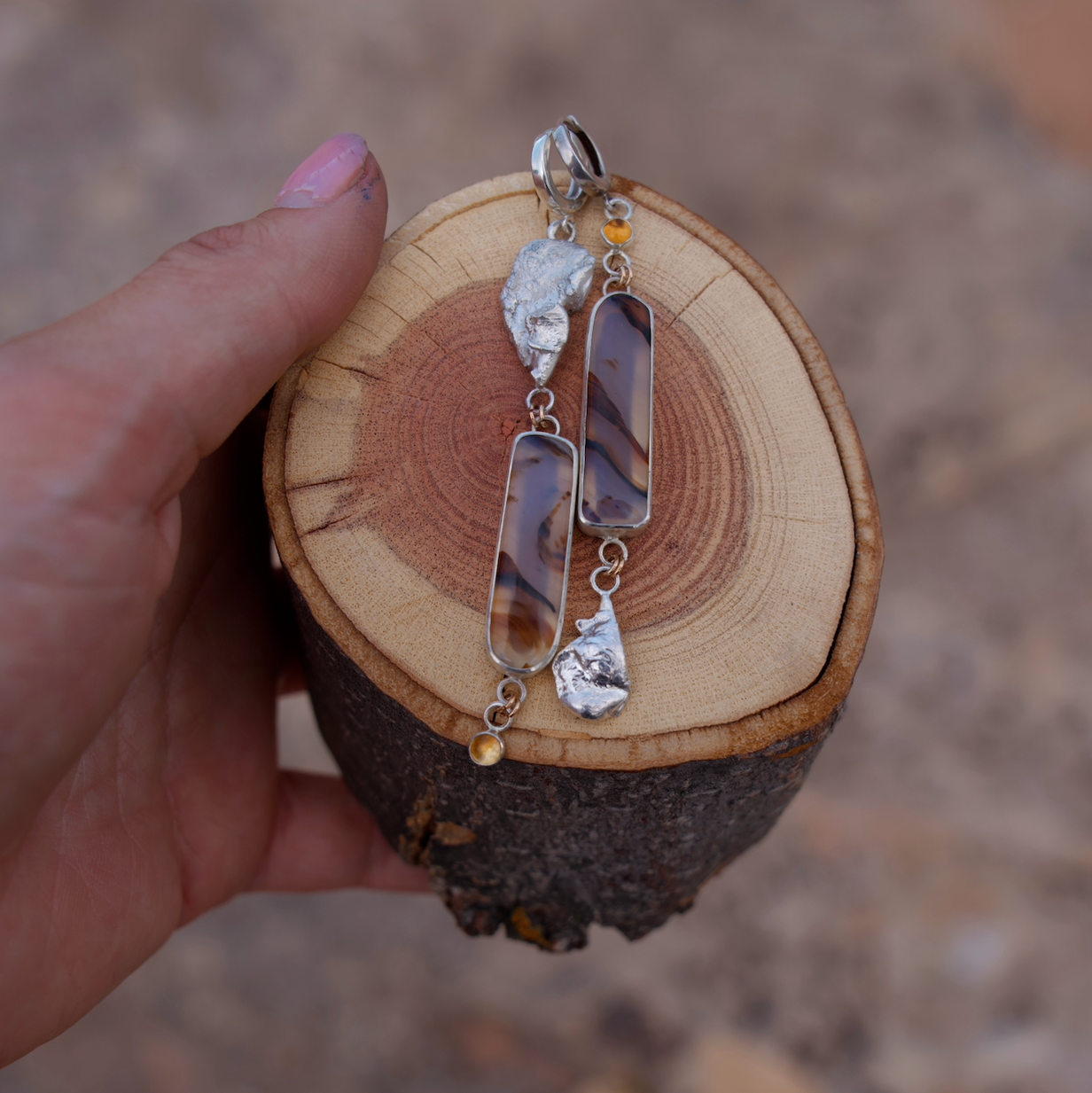 Silver earrings on a wooden block held by a hand with a blurred background